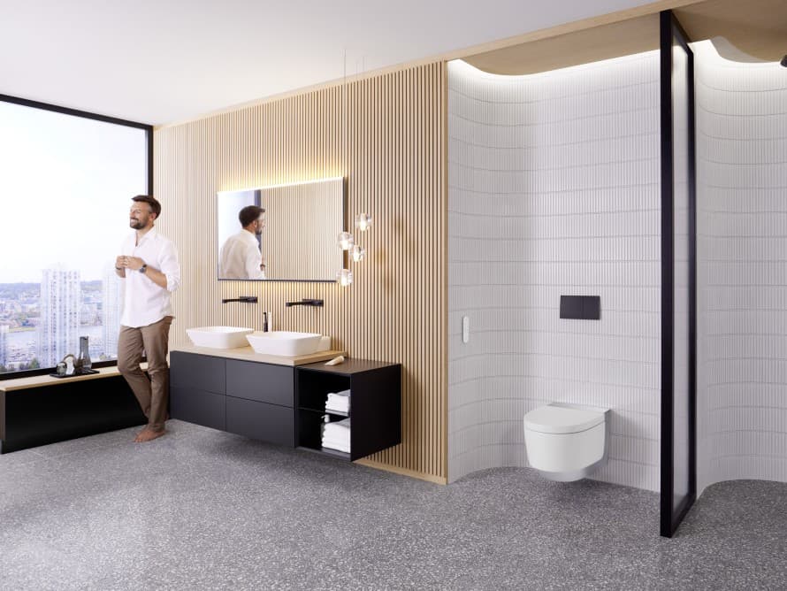 Oseba v veliki kopalnici s temnim pohištvom in Geberit AquaClean tuš WC-jem